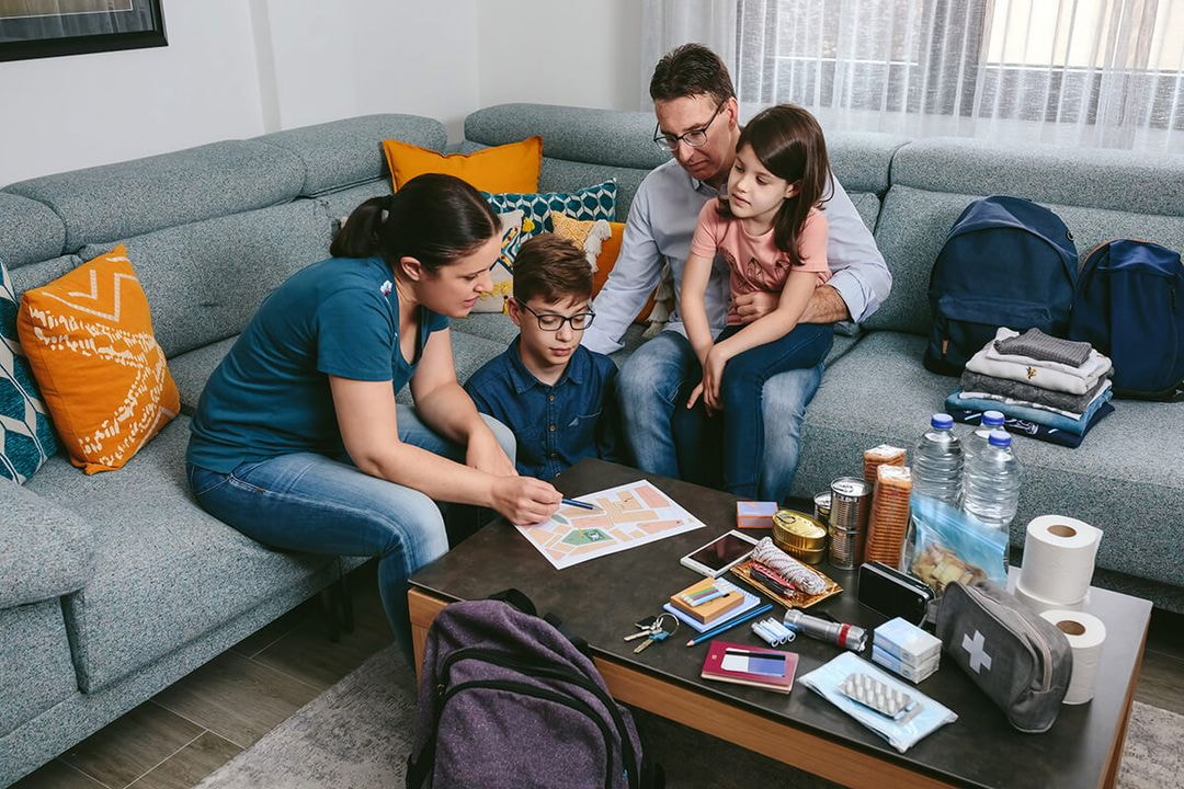 A family of four sits on a couch surrounded by their luggage, smiling and preparing for a trip together. 