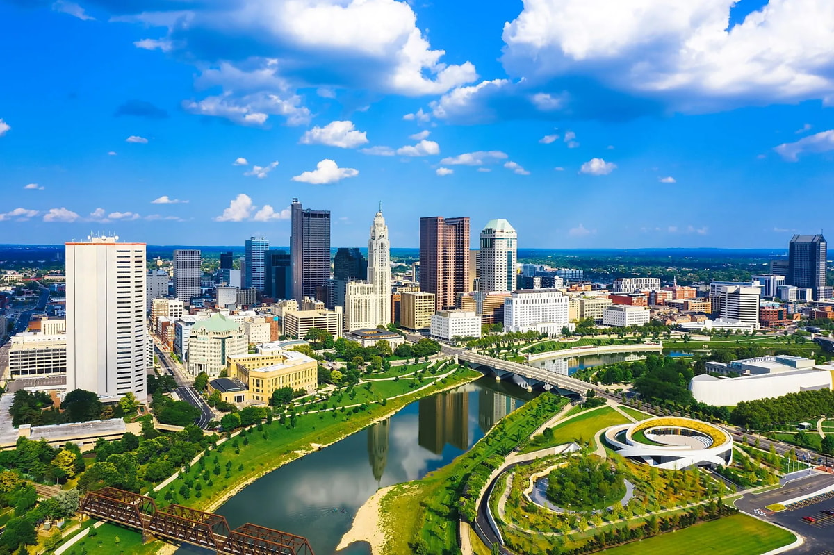 Aerial view of downtown Columbus, Ohio, showcasing skyscrapers and urban layout against a clear blue sky.
