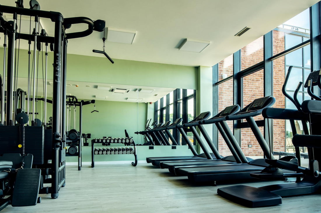 A gym room featuring several treadmills and large mirrors along the walls, creating a spacious workout environment.
