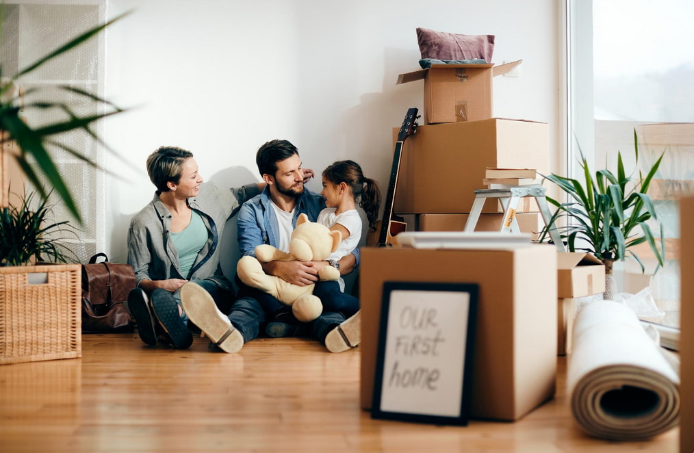 A family gathers on the floor, surrounded by unpacked boxes and furniture, as they settle into their new space.