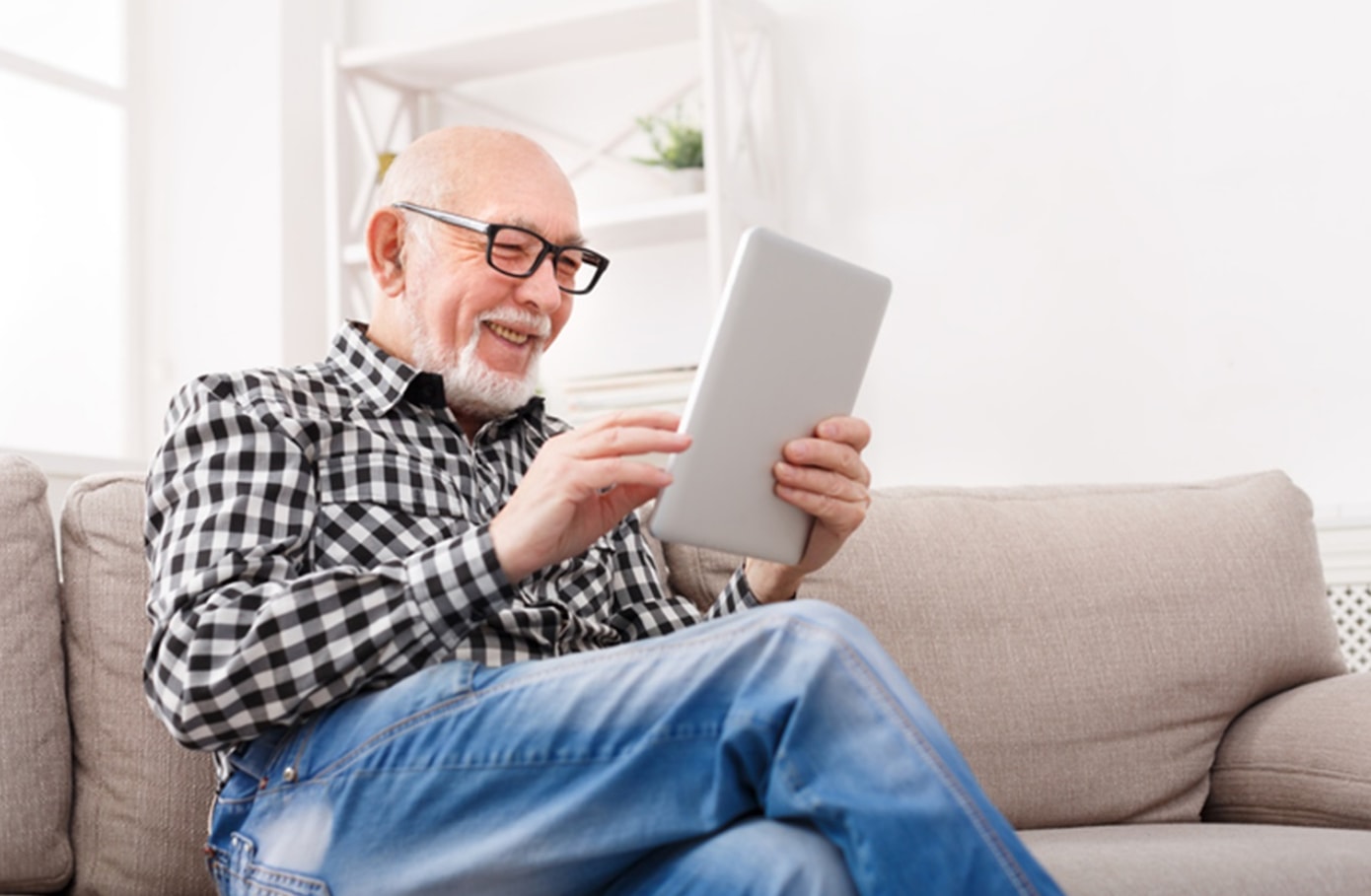 An older man sitting on a couch, focused on using a tablet computer in a cozy living room setting.