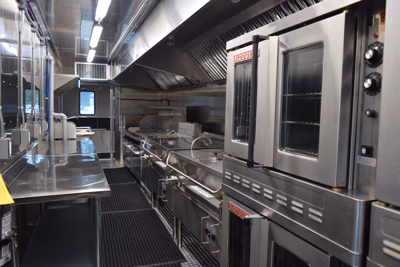 Interior of a clean, stainless steel commercial kitchen with ovens, stovetops, and worktables.