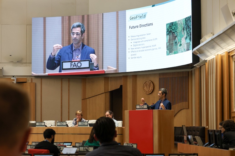 Ariel BenYishay is shown at a podium and on a screen addressing the GeoField convening.