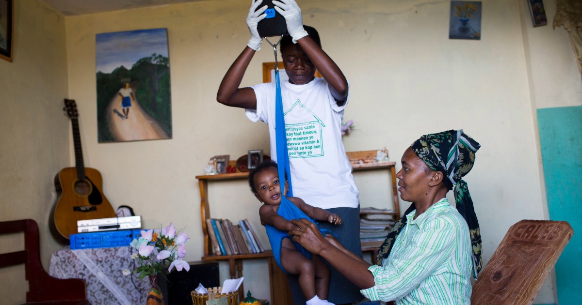 A community health worker in Haiti weighs a child during a home healthcare visit. USAID-provided tablets, made in a USAID-supported local factory, help health workers track patients and record accurate data. Photo by David Rochkind for USAID via Flickr, licensed under CC BY-NC 2.0. 