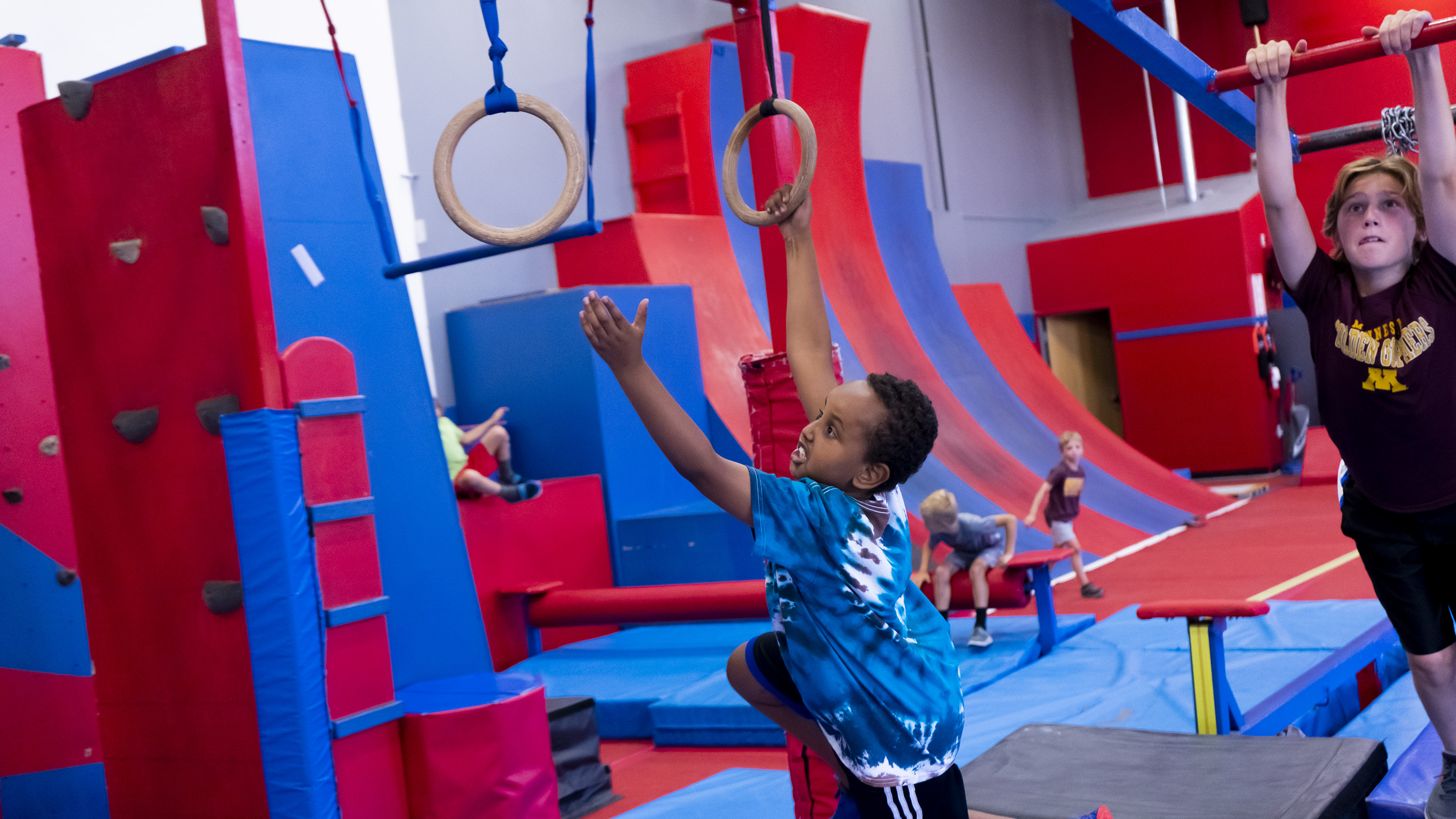 Boy climbing up a wooden platform at an indoor obstacle course.