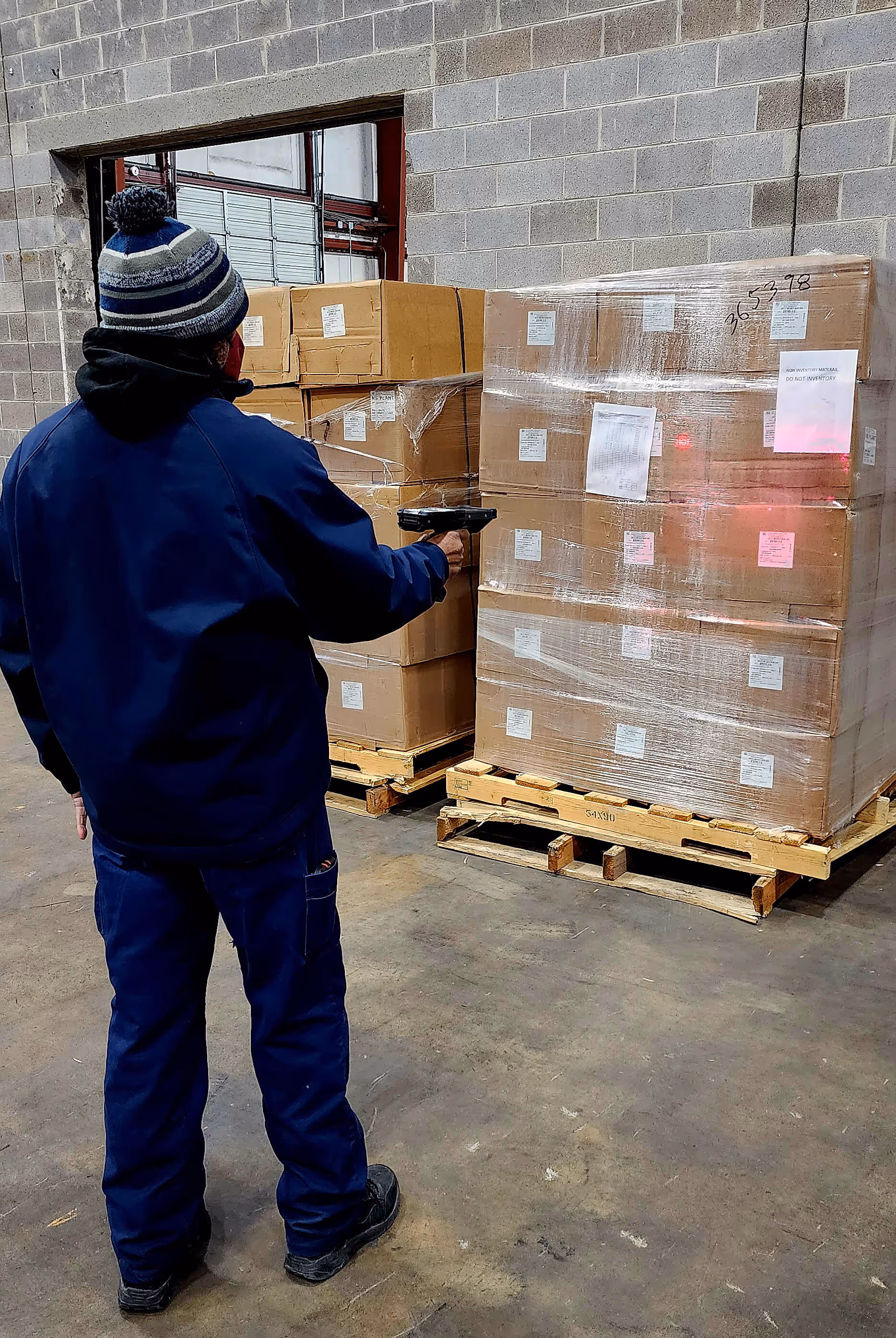 Warehouse worker scanning boxes wrapped in plastic on wooden pallets inside a storage area.