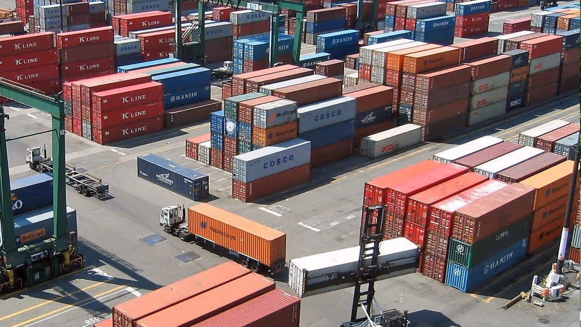 Aerial view of colorful stacked shipping containers and trucks at a busy port terminal.