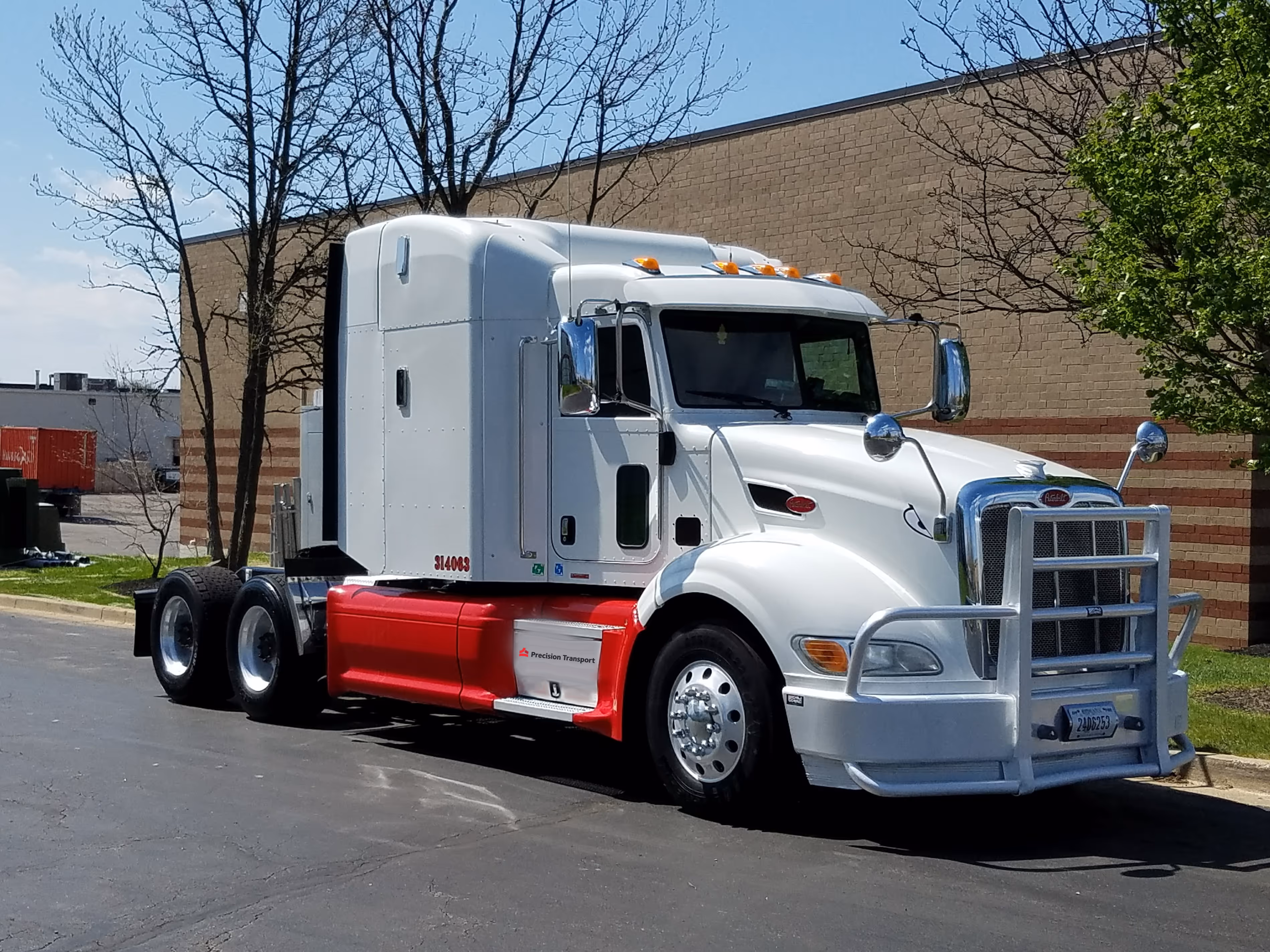 White and red semi-truck with sleeper cab parked on asphalt near a brick building.