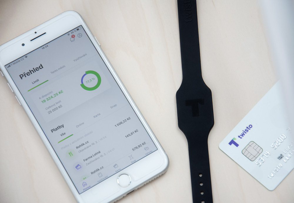 Twisto náramek ležící na stole vedle MasterCard karty a mobilu, na kterém běží Twisto aplikace.