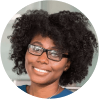 A smiling millennial black woman with a curly afro and glasses.