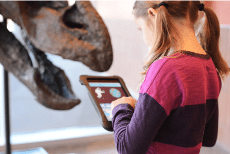 A young girl with pigtails facing a museum exhibit at the Arizona Science Center, using Ask Mode on an iPad. 