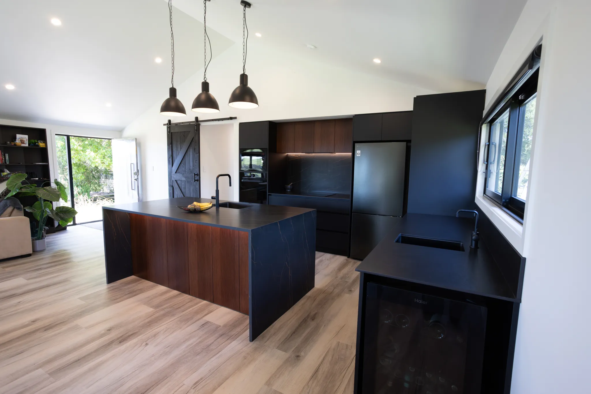 Modern kitchen with black countertops, a central island with wooden paneling, pendant lights, and light wood flooring.