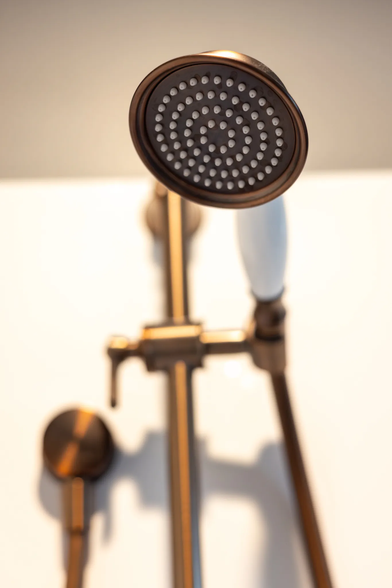 Close-up of a bronze showerhead with white handle on a wall-mounted shower fixture.