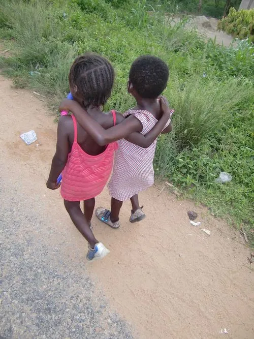 Två barn i Ghana som promenerar, foto taget snett bakifrån.