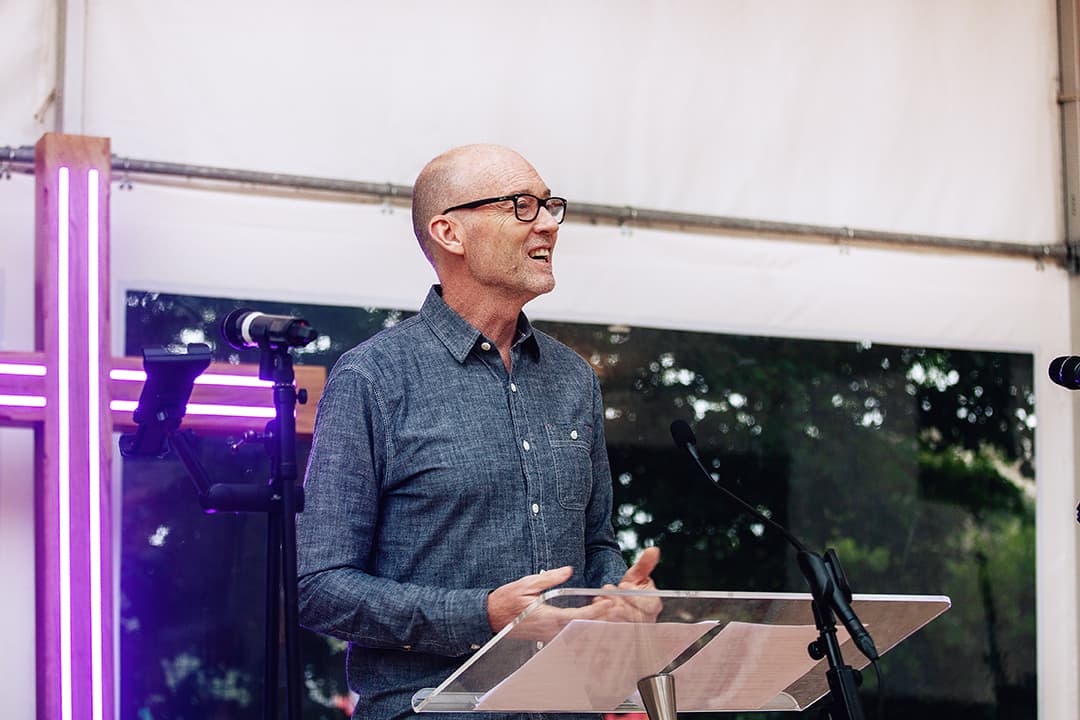 James Poch preaching in front of an illuminated cross