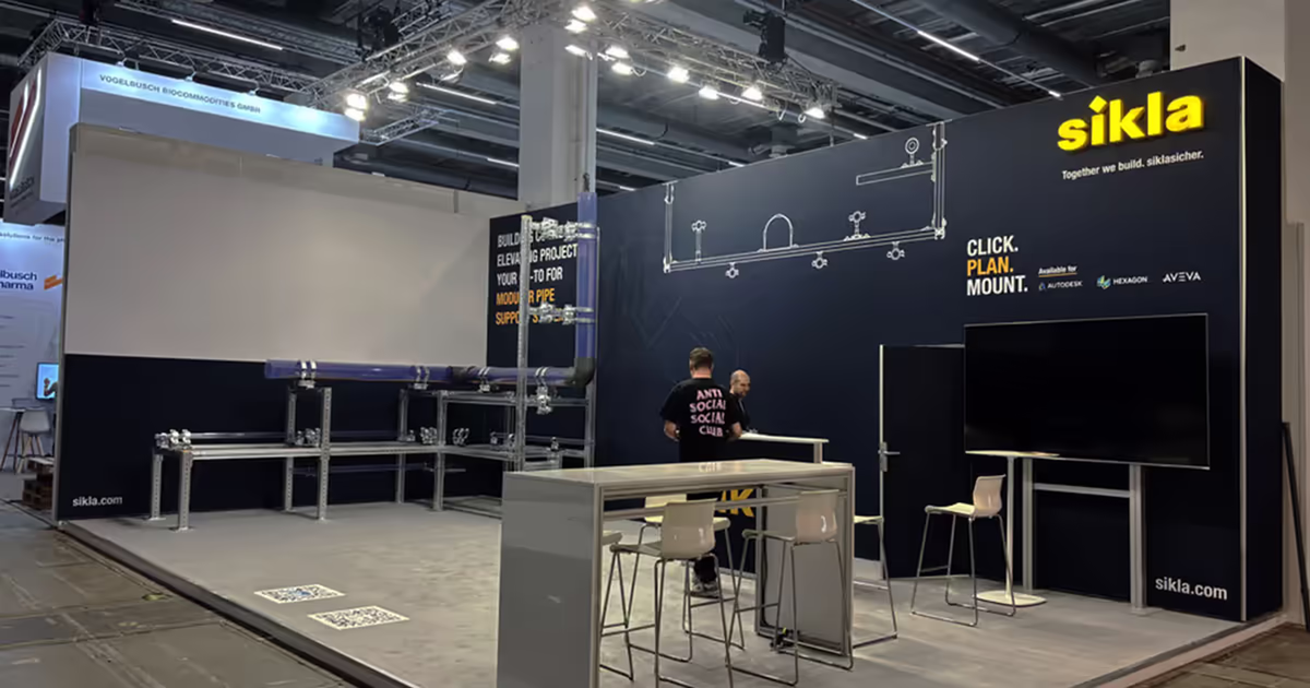 Messestand von Sikla mit großem schwarzen Hintergrund, Rohrleitungen als Ausstellungsstücke und Stehtischen mit Stühlen.