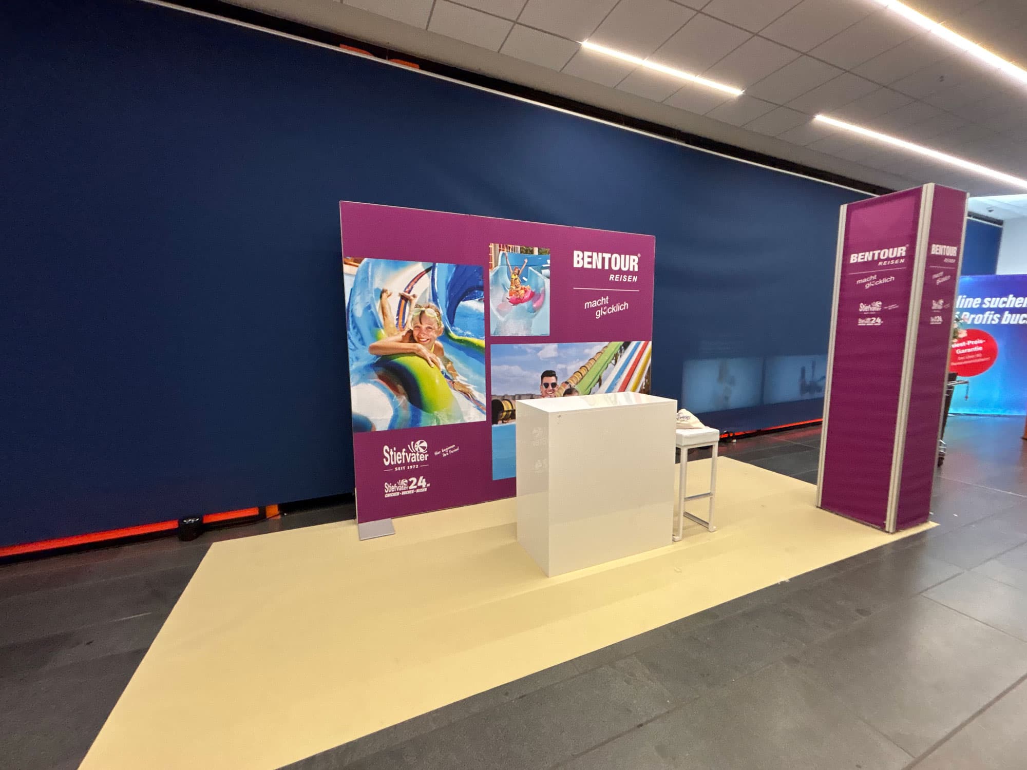 Kompakter Stand mit bedruckter Rückwand, weißer Theke und Branding-Säule bei der Hausmesse „Festival der Reisen“ 2025