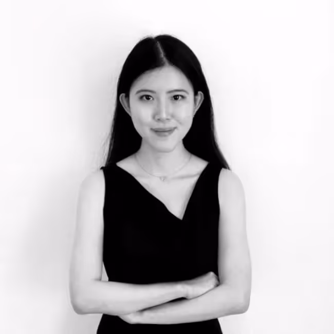 claudia natasia headshot - black and white photo of woman with long dark hair in dark dress with arms crossed against a white background