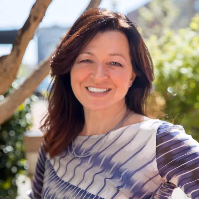 kara pernice headshot - woman with long reddish hair and striped purple shirt smiling against background of trees