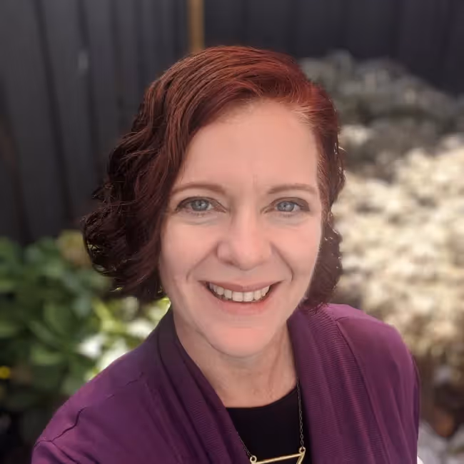 kassie chaney headshot - woman with red hair in purple shirt against natural background