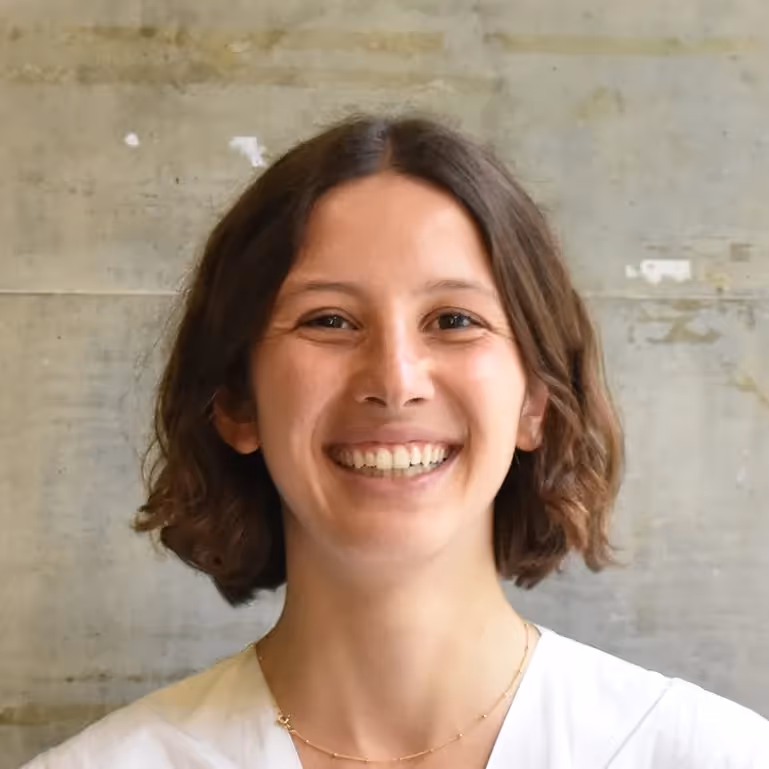 tyler Gindraux headshot - woman with short dark hair smiling in a white shirt against a gray background