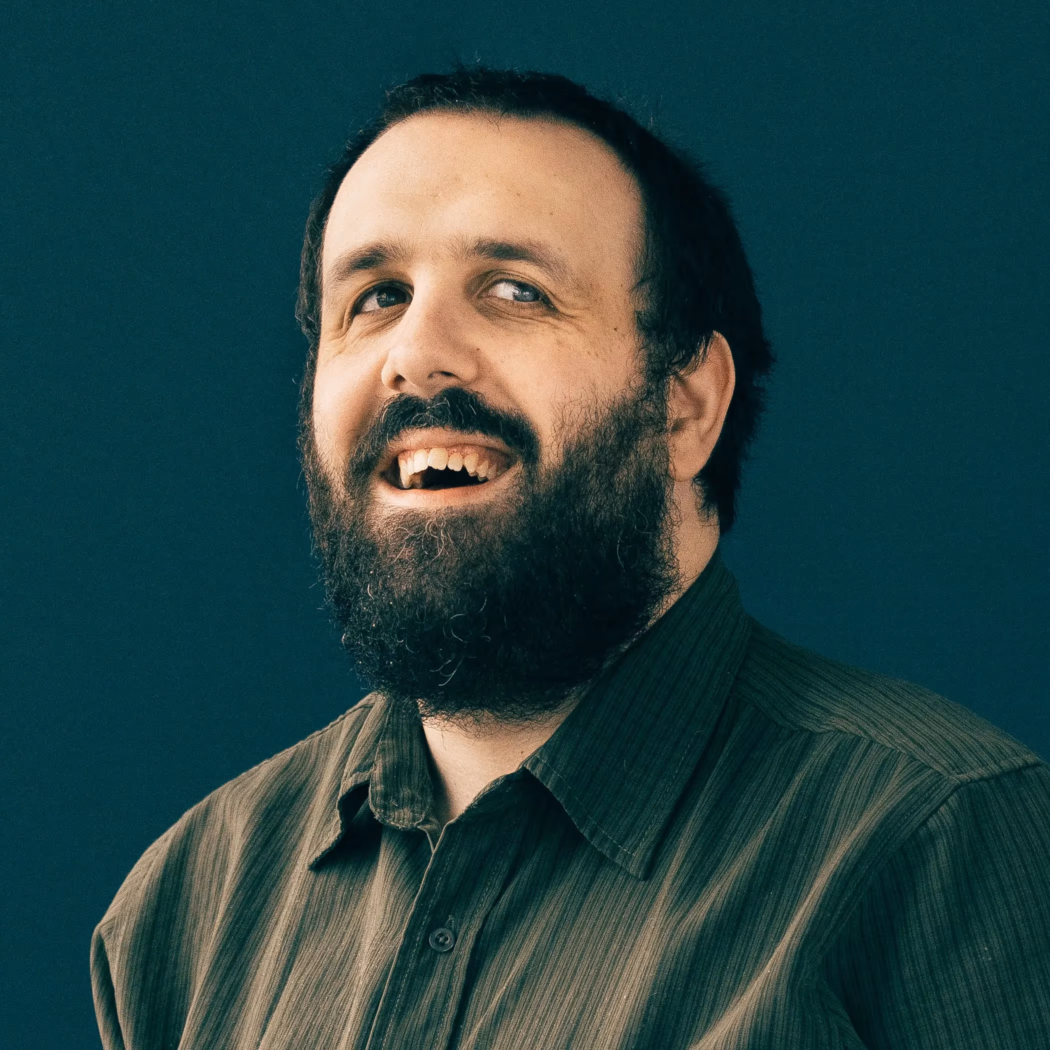 samuel proulx headshot - man with beard in green shirt against a dark background