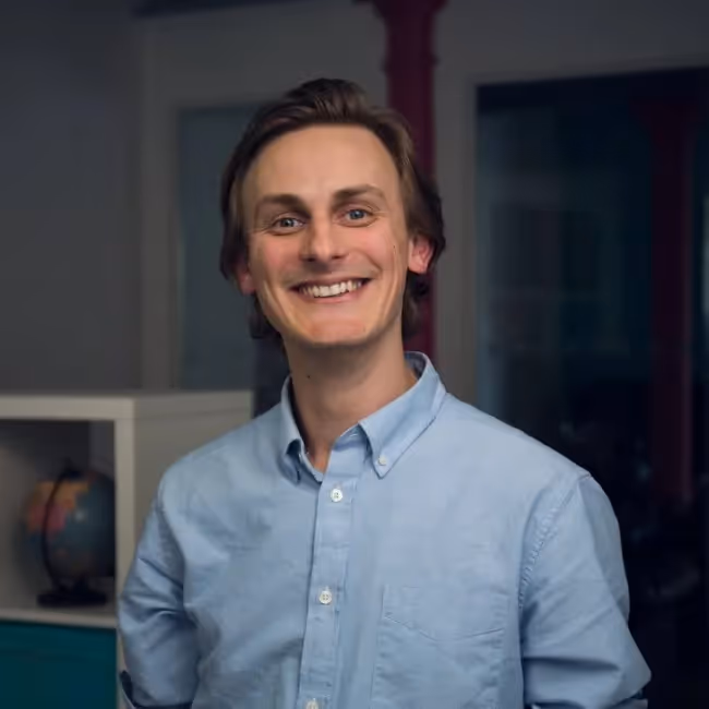 phil hesketh headshot - man in blue shirt standing against a dark background