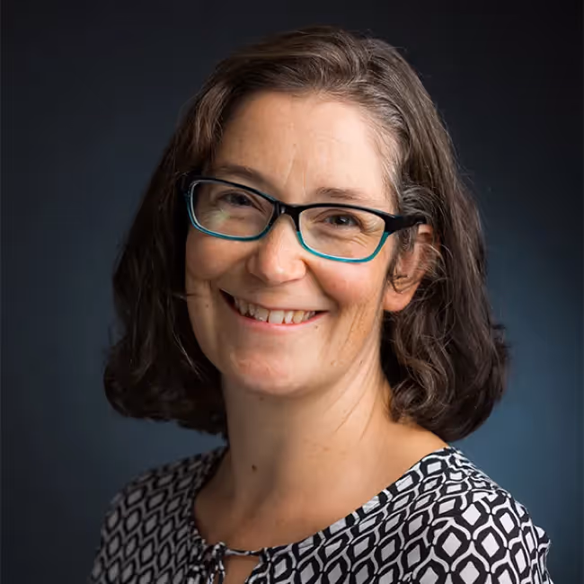 brigette metzler headshot - woman with short dark hair and glasses smiling against dark gray background