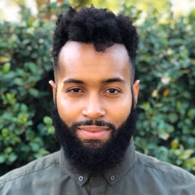 pierce Otlhogile-Gordon headshot - man with beard standing against a green background