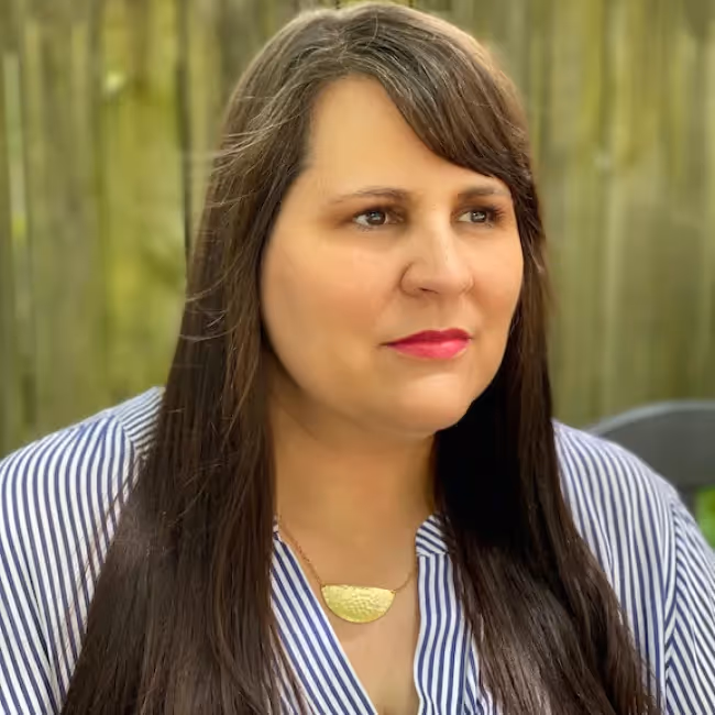 holly schroeder headshot - woman with long dark hair and bangs in purple shirt against plain background