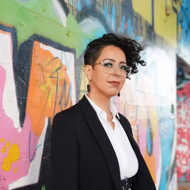 sarah fathallah headshot - woman with long dark hair and glasses against blue background