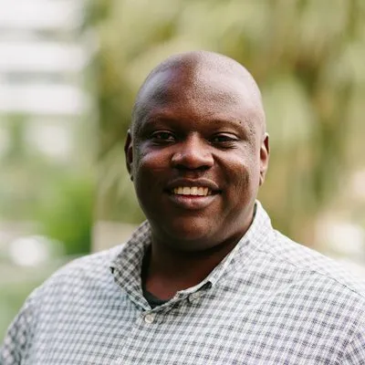 roy olende ux research headshot - man wearing checkered shirt with blurred green background