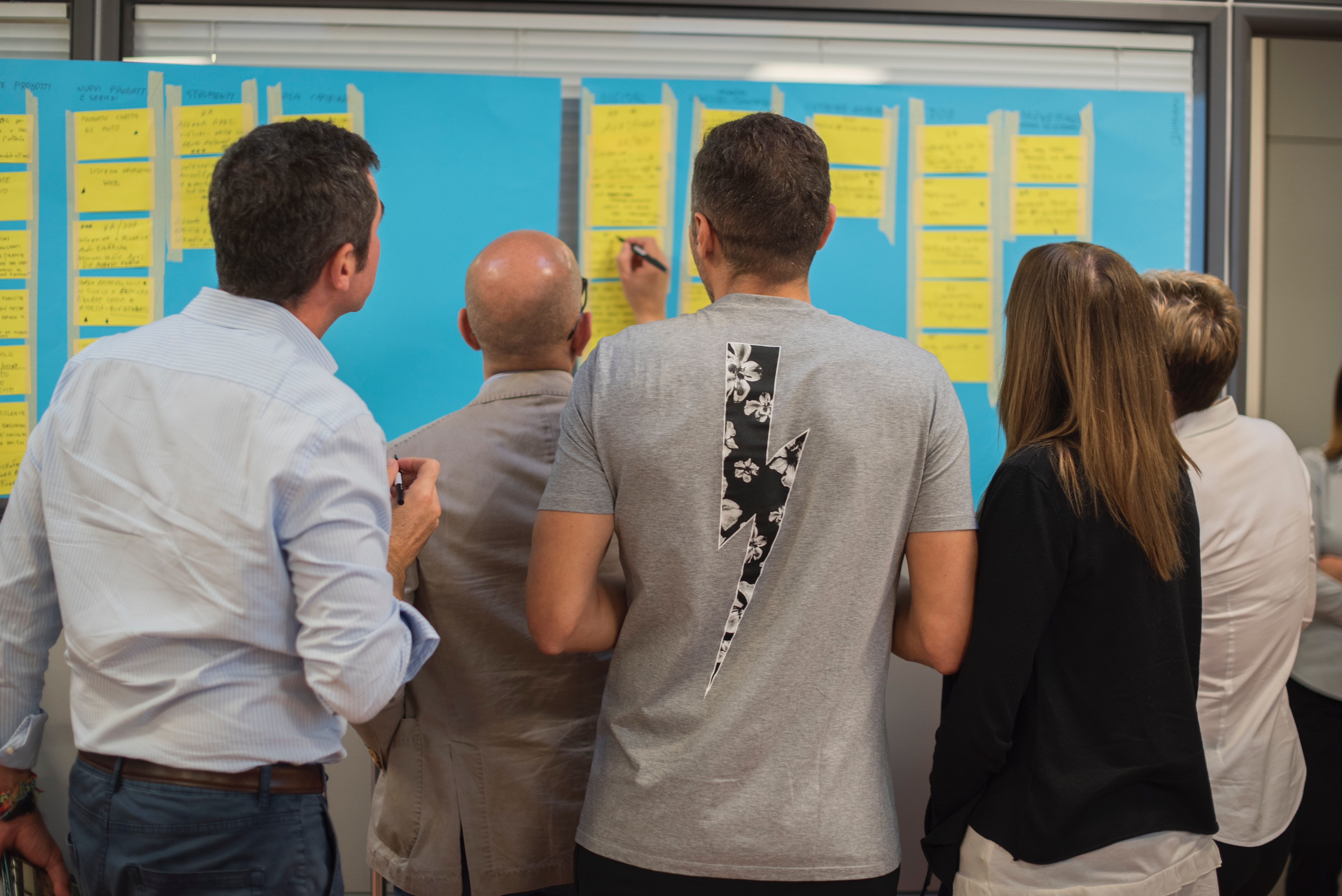 the backs of five people looking at a large poster with index cards