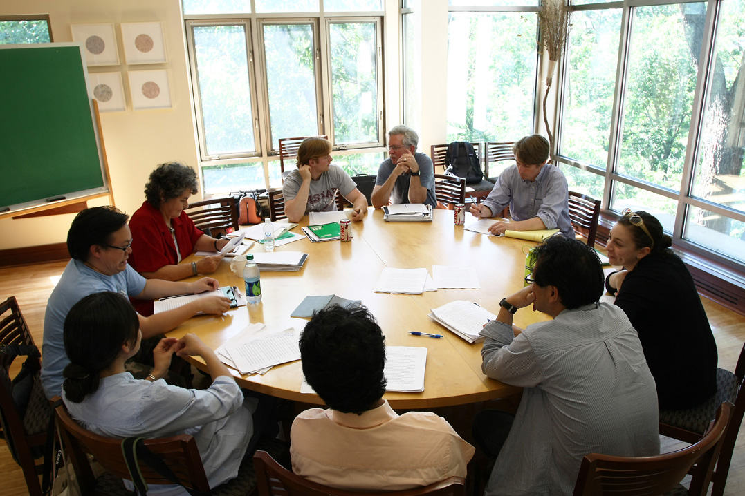 image of people sitting around a round table near a window with lots of papers spread out in front of them