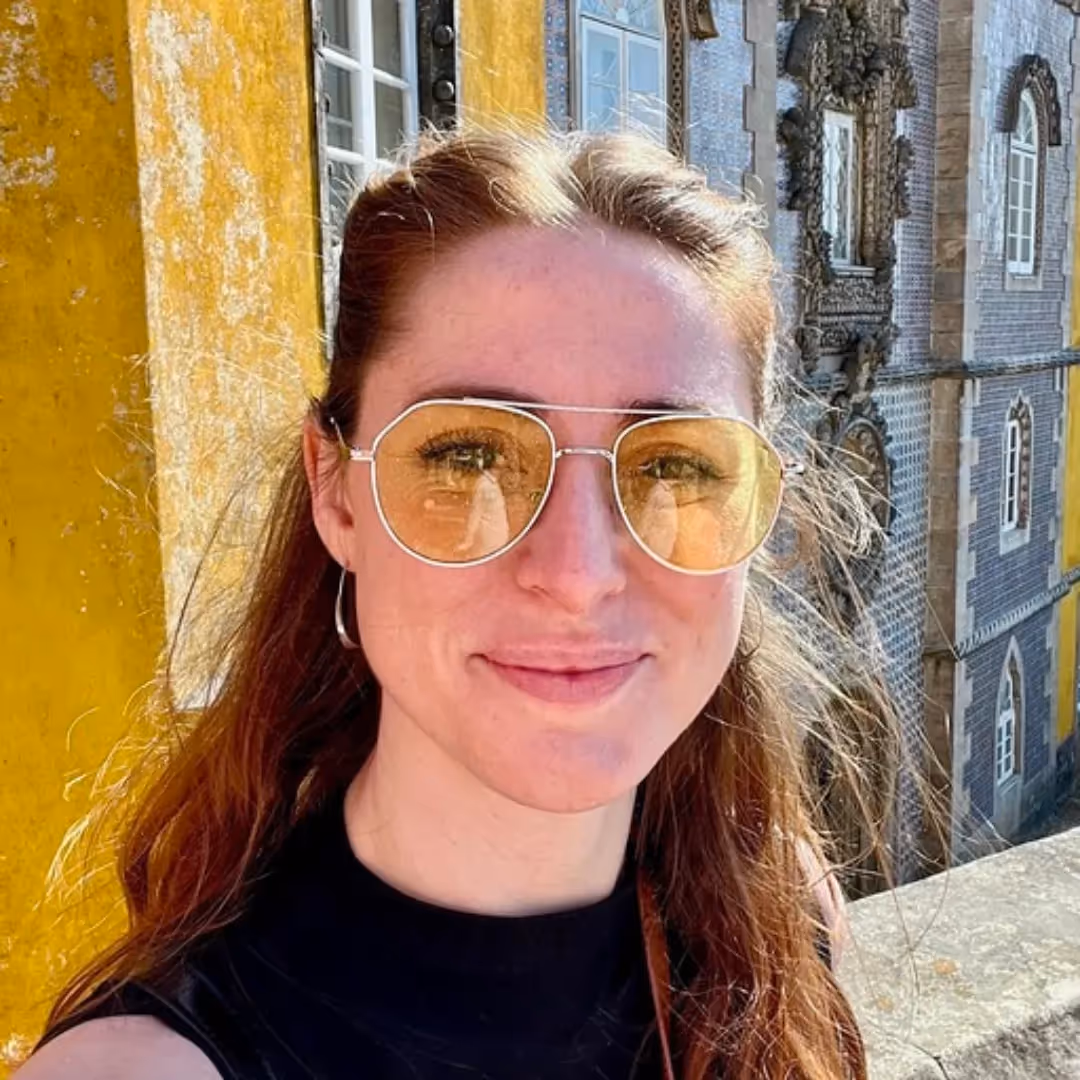 headshot for Katryna Balboni, a woman with brown hair posing with yellow sunglasses on