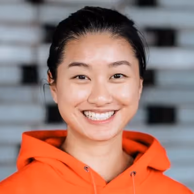A woman in an orange sweatshirt leaning against a pole and looking at the camera