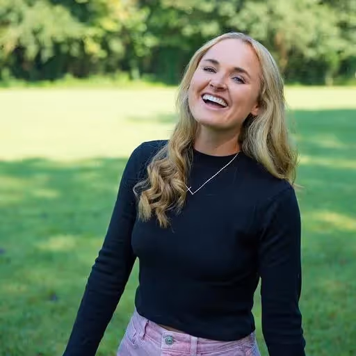 Photograph of Annie Mayfield wearing a black shirt with greenery in the background.