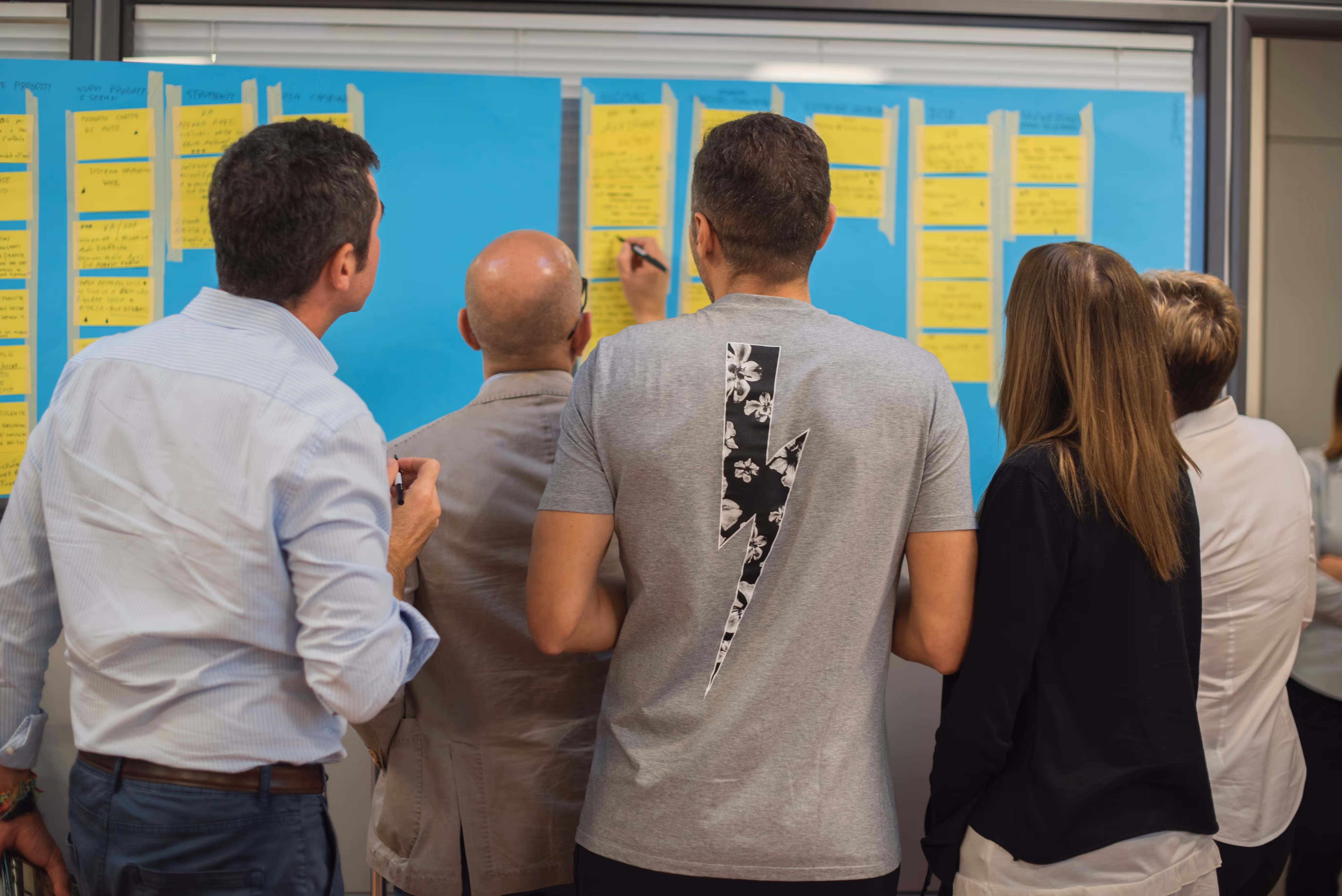 the backs of five people looking at a large poster with index cards