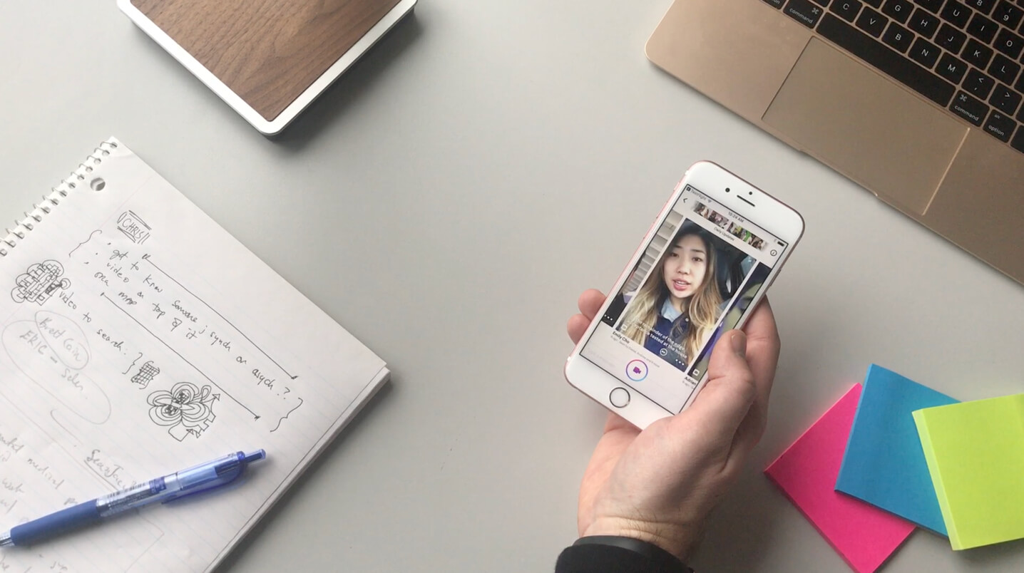 A photo over a desk of a hand holding the Helpful app on a phone with a laptop, pad of paper and sticky notes