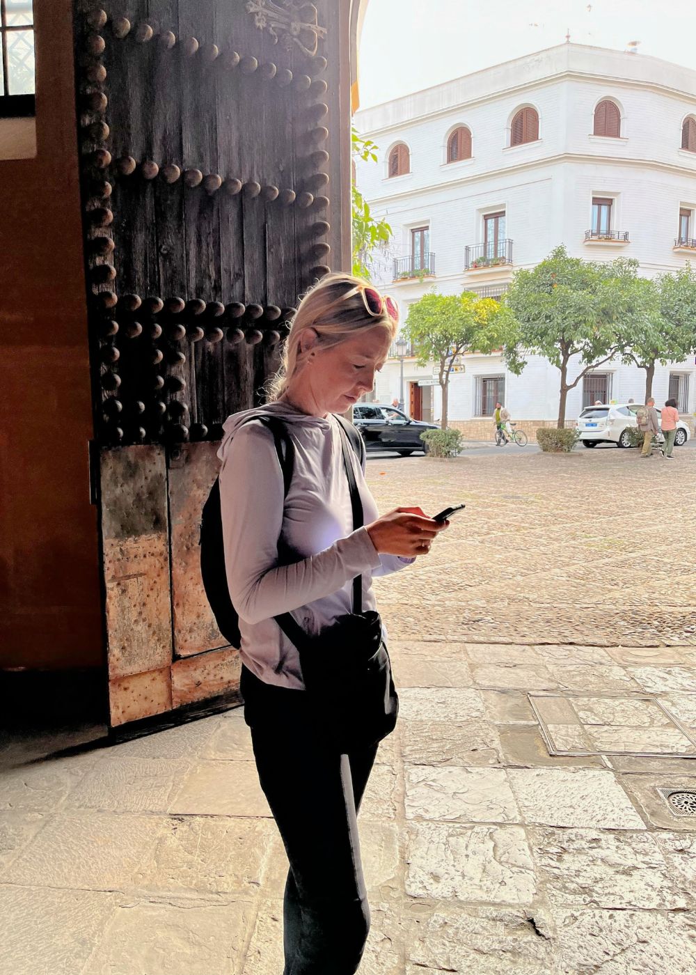 Author stands in Spanish courtyard, reading history on cell phone