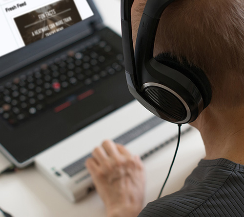 Person wearing headphones operating a refreshable braille display with a laptop in the background.