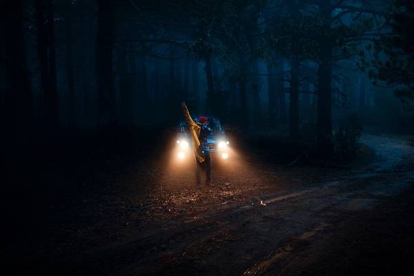 Man Standing Against Illuminated Car Headlights At Night