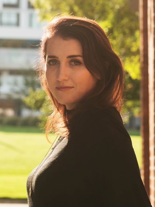 Professional portrait of Bethany standing against a yellow staircase.