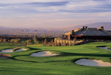 Anthem Golf course with sand bunkers and clubhouse overlooking a cityscape and mountains in the distance under a partly cloudy sky.