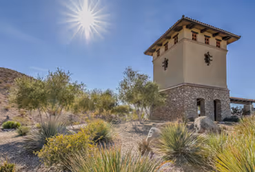 Desert landscape with a stone and stucco tower under a bright sun and clear blue sky.