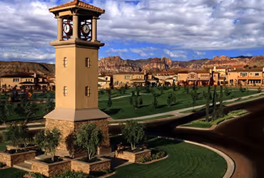Summerlin clock tower overlooking a landscaped green park with houses and mountains in the background under a partly cloudy sky.