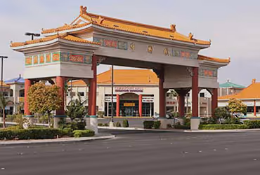Las Vegas Chinatown traditional Chinese-style archway with red pillars and decorative roof in front of a shopping center under clear blue sky.