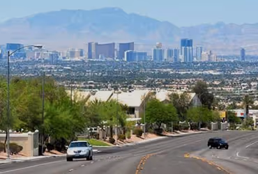 View of a North Las Vegas suburban street with cars driving and the Las Vegas skyline with mountains in the background.