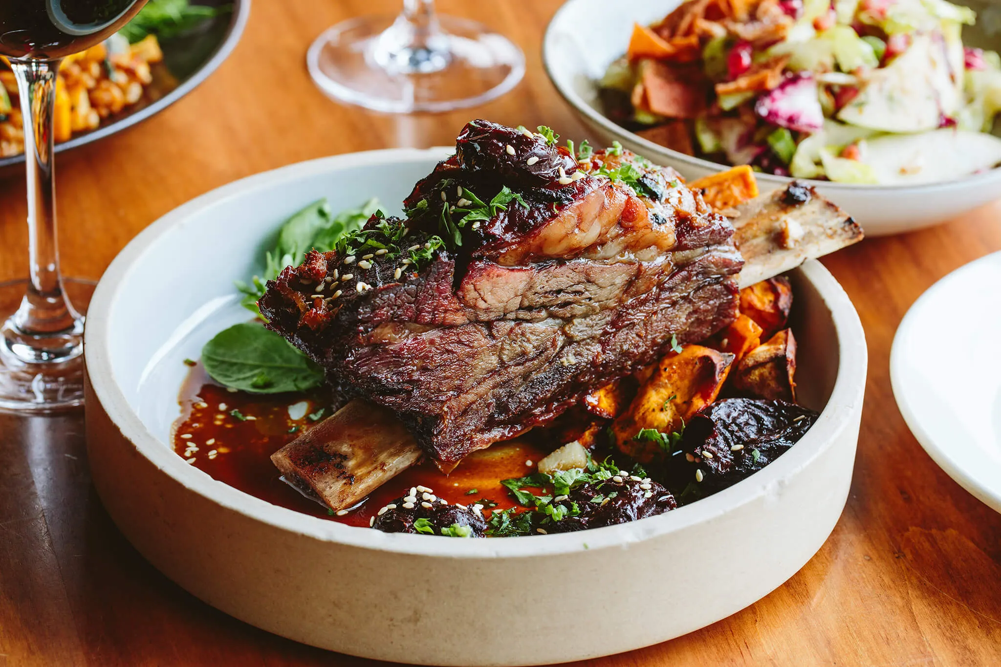 Plate with a braised beef short rib garnished with herbs, served on roasted vegetables and sauce.