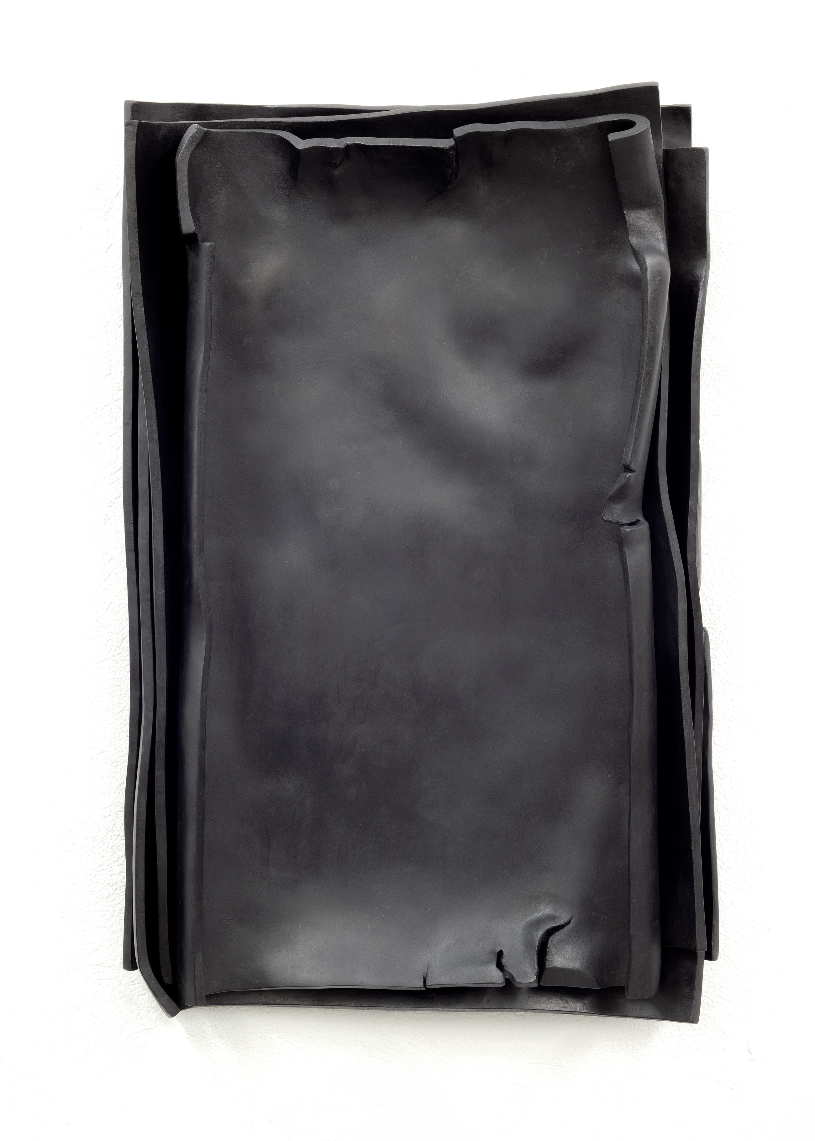 The sculpture entitled Besser Vertikal 11 by sculptor Erik Andersen is made of black epoxy resin and consists of several loose sheets stacked on top of each other, reminiscent of paper. The work hangs vertically on a white wall.